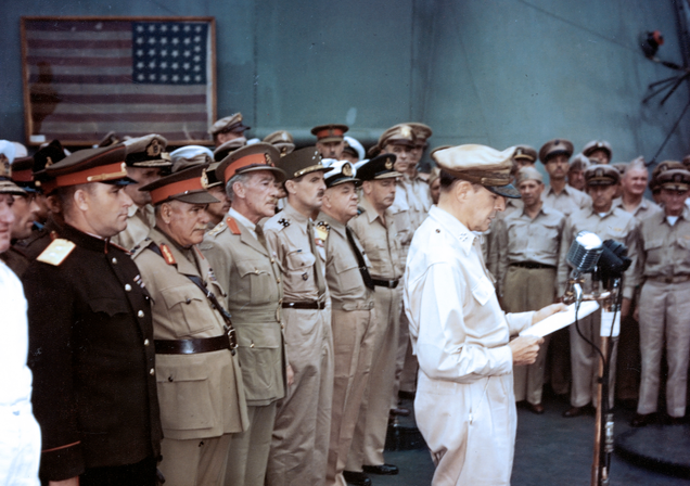 The Perry flag is visible in the background behind the assembled military dignitaries. General MacArthur is at the microphone. (US Navy)